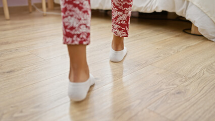 A woman in floral pajamas and white socks walks across a bedroom with wooden flooring, implying a...