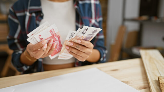 Woman counts icelandic krona in a carpentry workshop setting, conveying industry and finance.