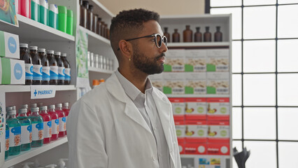 A professional african american male pharmacist in a white coat stands thoughtfully in a modern...