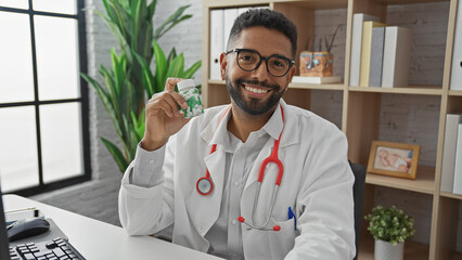 A cheerful african american male doctor in a clinic holding medication pills as he poses for the...