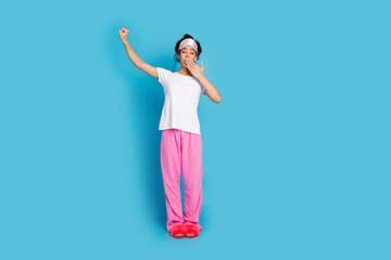 Full body portrait of pretty young woman stretch yawn empty space wear pajama isolated on blue...