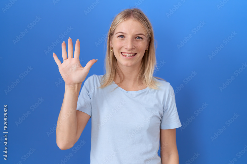 Poster young caucasian woman wearing casual blue t shirt showing and pointing up with fingers number five w