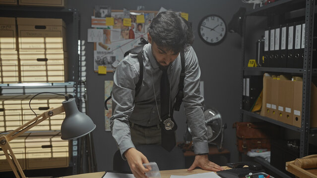 A bearded man in a detective's office examines evidence amidst file cabinets and a pinboard.