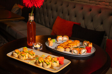 Close-up of sesame sushi with avocado and shrimp and baked sushi on a table with a flower in the interior of a cozy restaurant