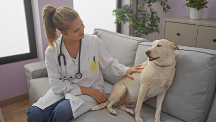 A woman in a white coat sitting on a couch examining a labrador in a cozy living room.