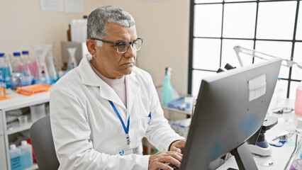 Mature man in lab coat working on computer in laboratory setting with scientific equipment.