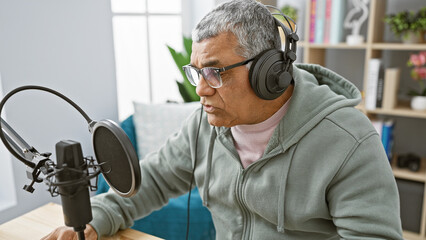 Mature grey-haired man with headphones speaking into microphone in a radio studio.