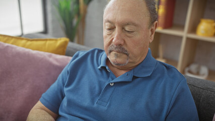 Middle-aged man with mustache in blue shirt resting on couch indoors, portraying relaxation at home.