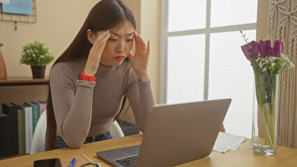 Stressed asian woman with headache working on laptop in home office