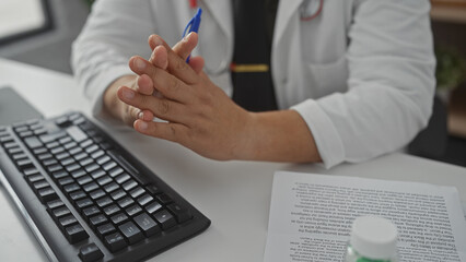 A hispanic man working indoors at a clinic with a computer, papers, and pens, portraying a...