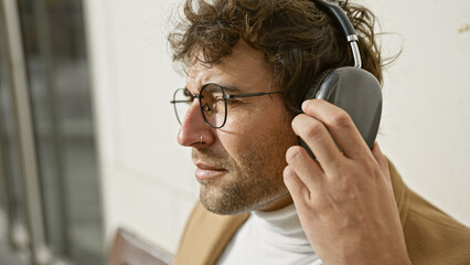 Handsome young hispanic man with beard enjoying music on headphones outdoors in an urban setting.