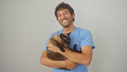 A smiling young man in a blue shirt affectionately holds a siamese cat against a white background.