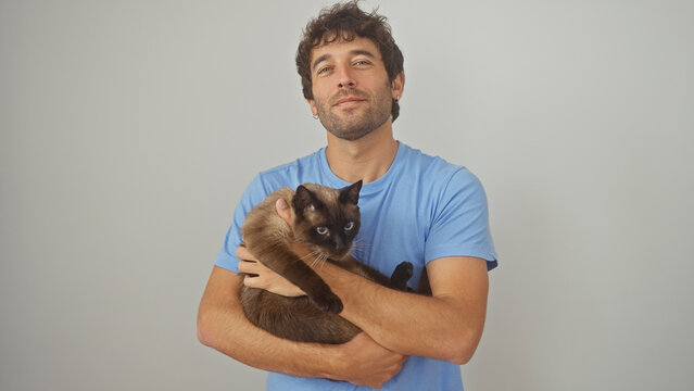 A contented young man embraces a siamese cat, both isolated on a clean white background.