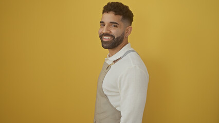 A cheerful young hispanic man with a beard posing confidently against a bright yellow background.