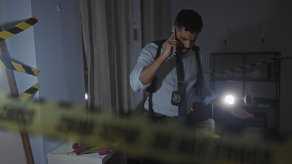 Hispanic detective investigates indoor crime scene at night, using flashlight, wearing badge and...