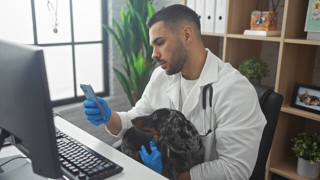 Hispanic male veterinarian using a mobile phone while holding a teckel dog in a clinic setting.
