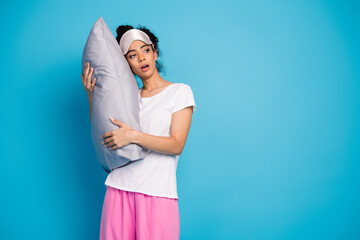 Portrait of pretty young woman hold pillow look empty space wear pajama isolated on blue color...