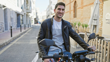 Handsome hispanic man in leather jacket smiling on motorcycle in sunny urban street scene.