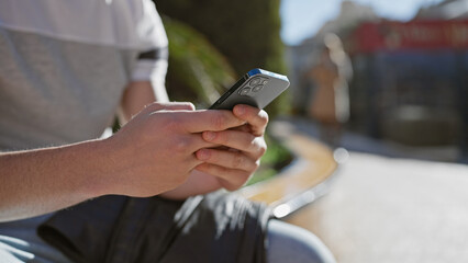 Close-up of a young hispanic man holding a smartphone in an urban outdoor setting, focused and...