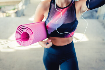 Happy young sporty woman carrying her workout equipment. Close-up of woman holding yoga mat outdoors. Unrecognizable woman carrying mat for training. Fitness concept.