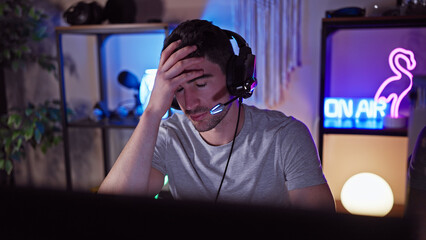 A young hispanic man distressed in a dark gaming room wearing headphones at night