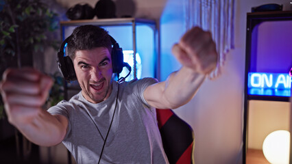 A young hispanic man celebrating joyfully in a dark gaming room with an 'on air' sign in the...