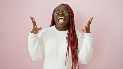 A joyful black woman with braids shouting and raising her hands against a pink background