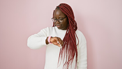 African american woman with braids wearing glasses checks time on pink background
