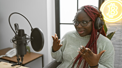 African american woman with braids speaking into a microphone in a radio studio, wearing glasses...