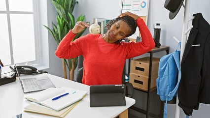 African american woman stretching in a modern office interior with a laptop and plant.