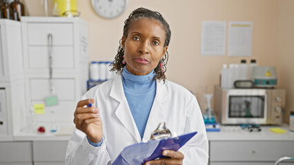 African american woman scientist with clipboard in lab assessing a specimen in a hospital...