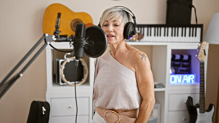 Mature woman singing in a music studio with microphone, headphones, and guitars