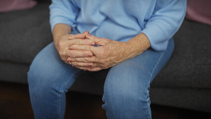Elderly woman sitting indoors calmly with hands clasped, exuding serenity and contemplation.