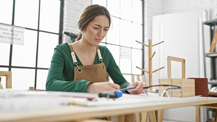 Woman carpenter working meticulously in a bright workshop with tools and wooden furniture around...