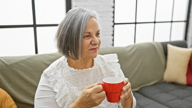 Mature woman holding coffee mug sitting in living room on couch