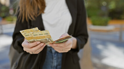 A young woman counts norwegian kroner on a sunny urban street.