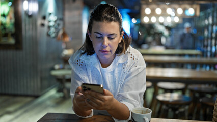 Beautiful young hispanic woman using smartphone at cafeteria