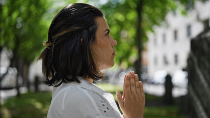 Obraz premium Beautiful young hispanic woman praying and mourning by tombstone at graveyard