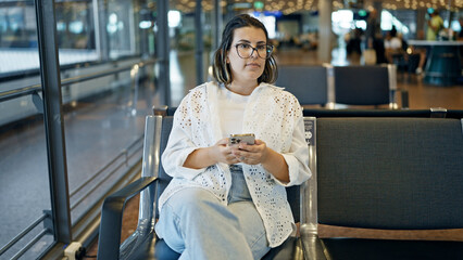 Beautiful young hispanic woman using smartphone at the airport