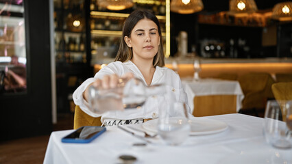 Young beautiful hispanic woman pouring a glass of water at the restaurant