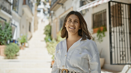 Fototapeta premium Young beautiful hispanic woman standing smiling at typical spanish old town