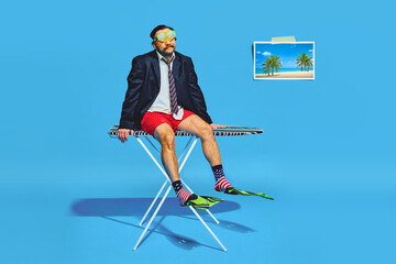 Man dressed in half in business attire and diving mask sitting on ironing against blue background. Summer moo Concept of pop art, remote work, travelling, party, recreation, lifestyle, fashion, style.