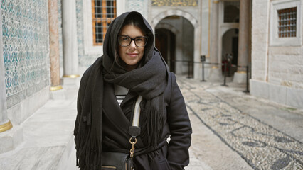 A young woman in stylish eyewear and scarf poses at topkapi palace, istanbul, hinting at history...
