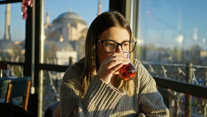 Young woman drinking tea in a restaurant overlooking hagia sophia in istanbul, turkey