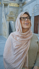 A smiling woman in a hijab stands inside an ornate istanbul mosque, embodying cultural appreciation.