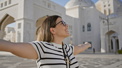 Happy woman with arms open in front of the grand qasr al watan in abu dhabi, embodying travel and...