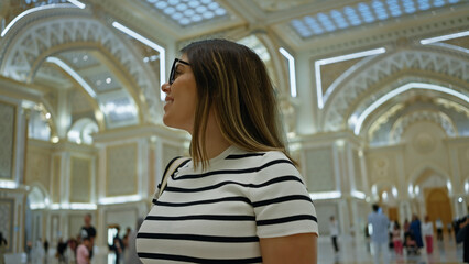 A young woman tours the ornate interior of abu dhabi's qasr al watan palace, reflecting the rich...