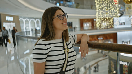 Smiling young woman with glasses inside a luxurious dubai mall, surrounded by elegant shops.
