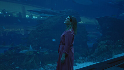 A young adult woman enjoys the underwater view at a dubai aquarium, showcasing tourism and marine life.