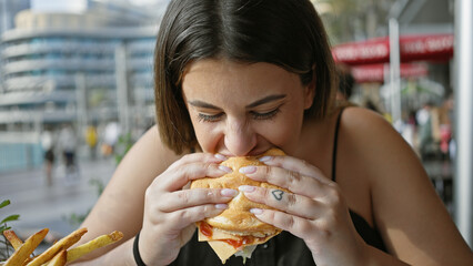 Young woman eating burger outdoor with city background enjoying fast food.
